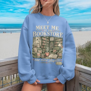 Light blue sweatshirt with "Meet Me at the Bookstore" text and book illustrations.