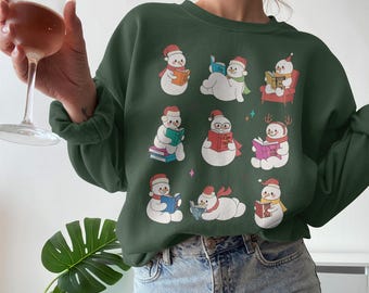 May include: A dark green sweatshirt with a pattern of snowmen reading books. Each snowman wears a red hat and scarf, with some seated or reclining. The design includes colourful books and a few small stars.
