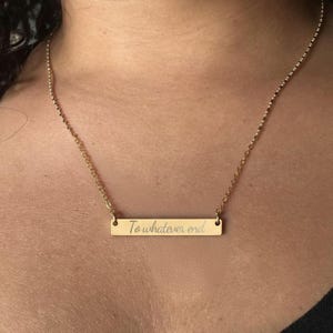 A gold-colored necklace with a rectangular pendant that says "To whatever end".