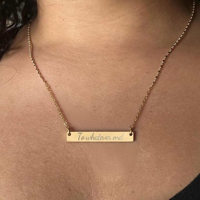 A gold-colored necklace with a rectangular pendant that says "To whatever end".