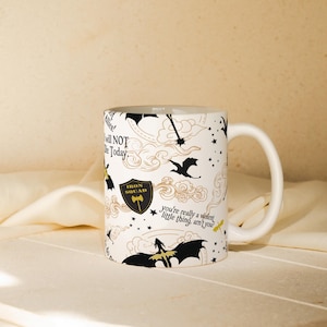 May include: White ceramic mug with a wraparound design featuring dragons, stars, and text. The mug has a curved handle and is decorated with the words "Iron Squad" and "You're really a violent little thing, aren't you?"