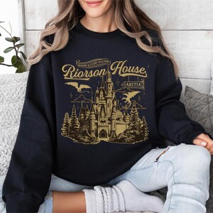 a woman sitting on a couch wearing a black shirt with a castle on it
