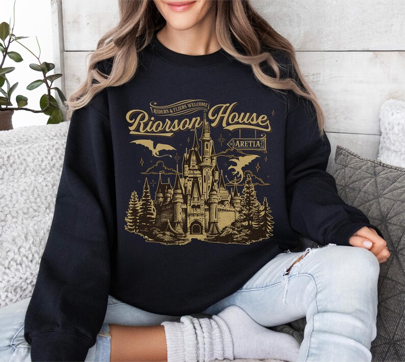 a woman sitting on a couch wearing a black shirt with a castle on it