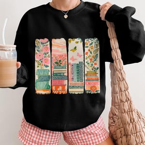 Black sweatshirt with colorful stacked books and floral designs.