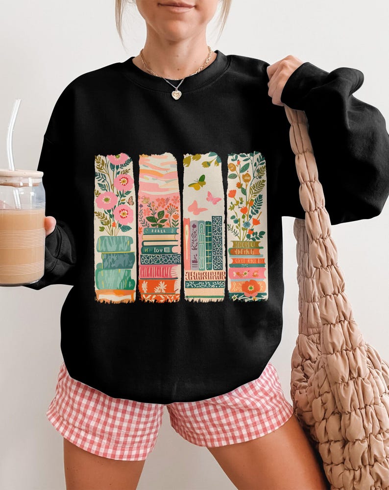 Black sweatshirt with colorful stacked books and floral designs.
