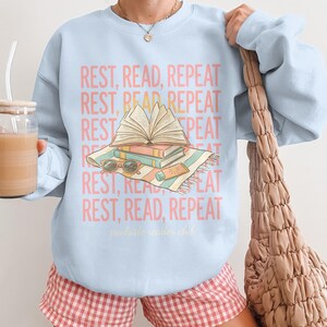 Light blue sweatshirt with "REST, READ, REPEAT" text and "poolside reader club" logo.