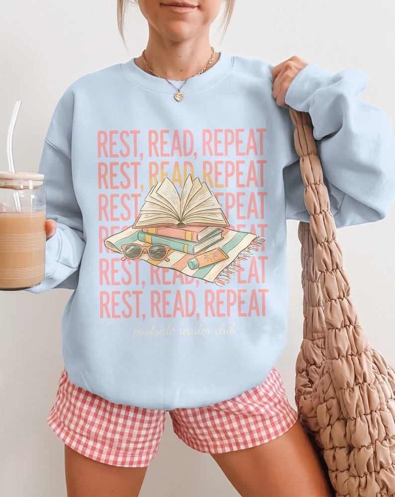 Light blue sweatshirt with "REST, READ, REPEAT" text and "poolside reader club" logo.