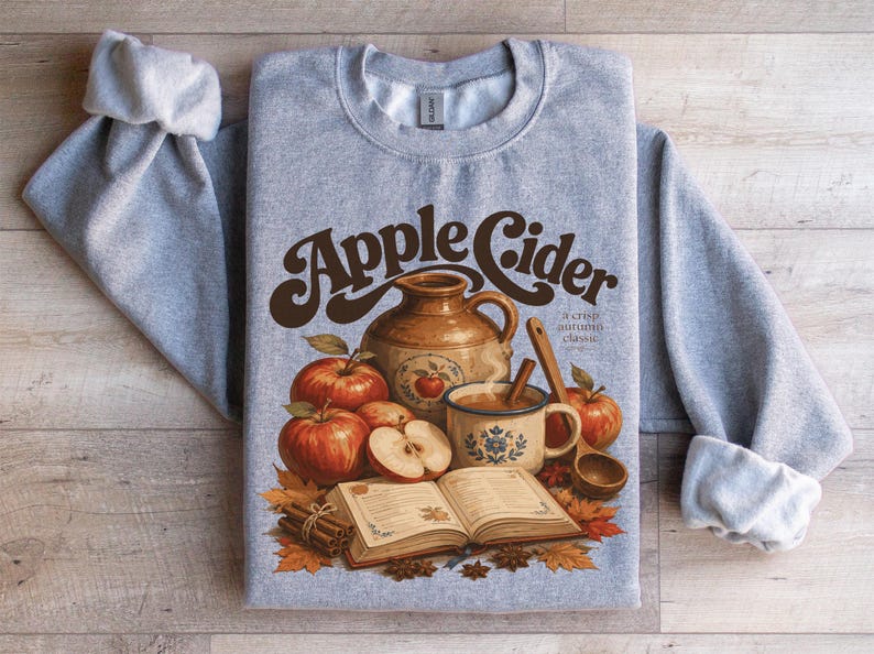 Grey sweatshirt with "Apple Cider" graphic featuring apples, a jug, and cinnamon sticks.