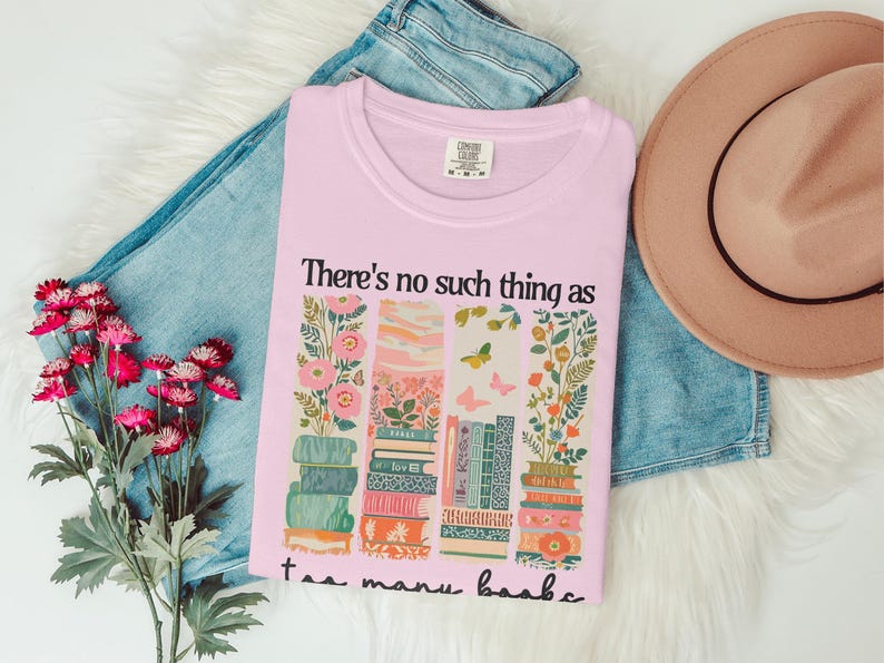 Pink t-shirt with floral and book design and text "There's no such thing as too many books."