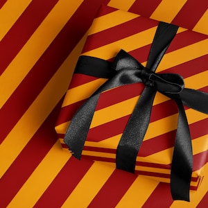 May include: A wrapped gift box with a black satin bow. The gift wrap features a pattern of diagonal red and yellow stripes. The gift box is placed on a matching wrapping paper background.