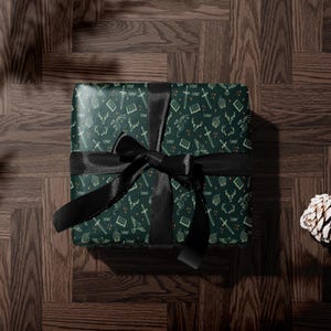 A green gift box with a black ribbon tied around it, placed on a wooden surface.