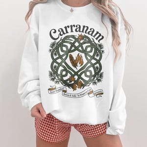 White sweatshirt with intricate knotwork, feathers, and text "Carranam".