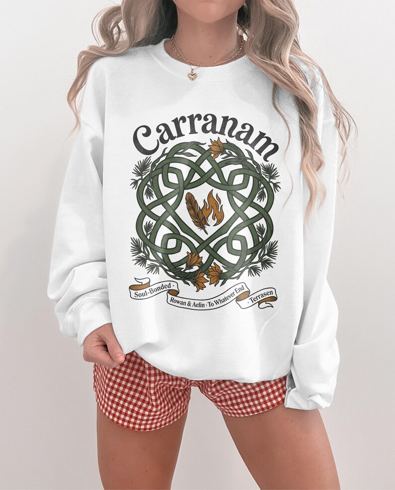 White sweatshirt with intricate knotwork, feathers, and text "Carranam".