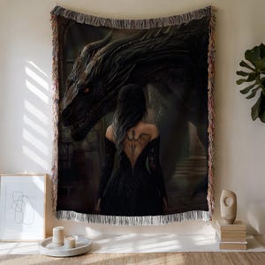 May include: Woven tapestry depicting a fantasy scene with a woman in a black dress and a large black dragon. The tapestry has a fringed edge and is displayed on a wall. The woman has a dragon tattoo on her back.