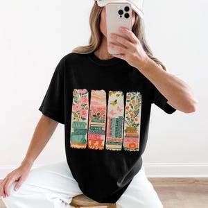Black t-shirt with four stacked rows of colorful books featuring floral patterns.