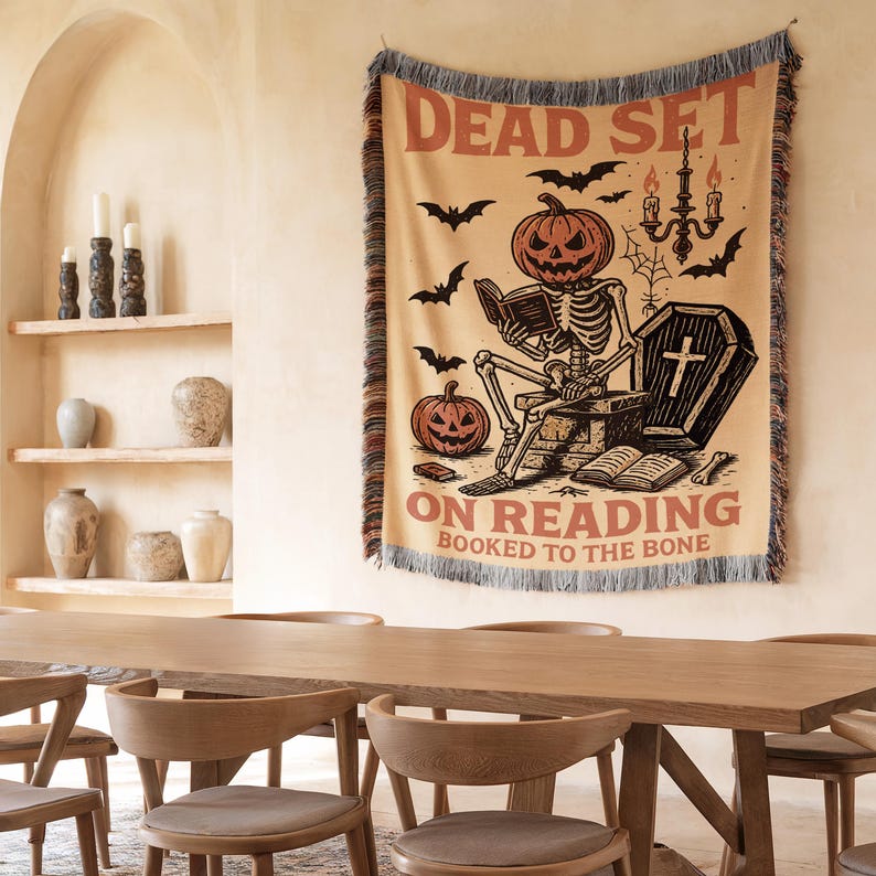 a Halloween-themed tapestry hanging on a wall, depicting a skeleton reading a book and a skull with a cross, with the text "Dead Set on Reading" below the illustration.