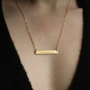 A gold necklace with a rectangular pendant that says "To whatever end".
