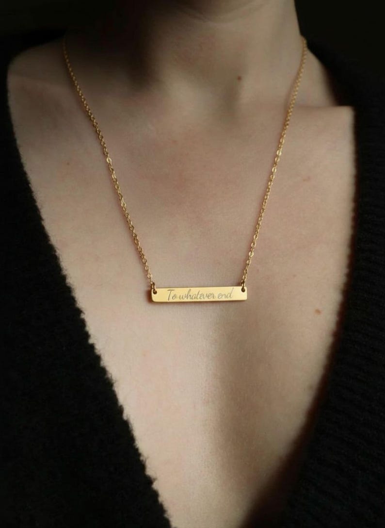 A gold necklace with a rectangular pendant that says "To whatever end".
