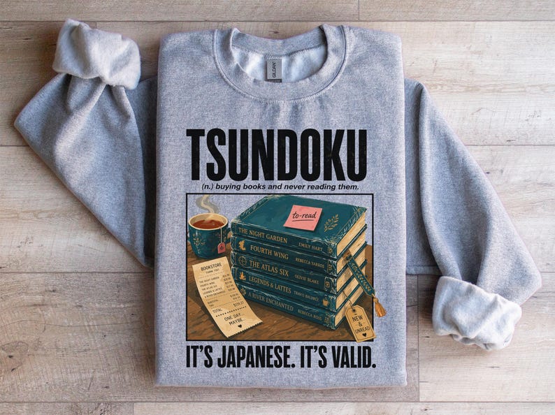 Gray sweatshirt with "Tsundoku" definition and stack of books.
