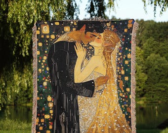 May include: A woven throw blanket featuring a romantic illustration of a couple embracing and kissing. The artwork has a dark background with gold and yellow accents, and the couple is depicted in black and gold. The blanket has a fringed edge.