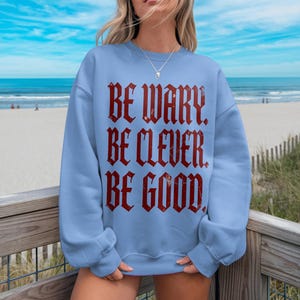 Light blue sweatshirt with distressed red text reading "BE WARY. BE CLEVER. BE GOOD."