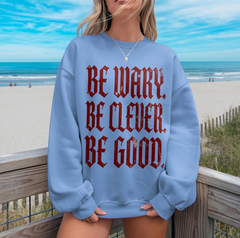 Light blue sweatshirt with distressed red text reading "BE WARY. BE CLEVER. BE GOOD."