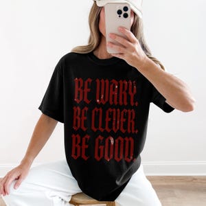 Black t-shirt with red distressed text "BE WARY. BE CLEVER. BE GOOD."