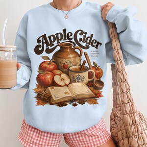 "Apple Cider a crisp autumn classic" graphic on light blue sweatshirt.