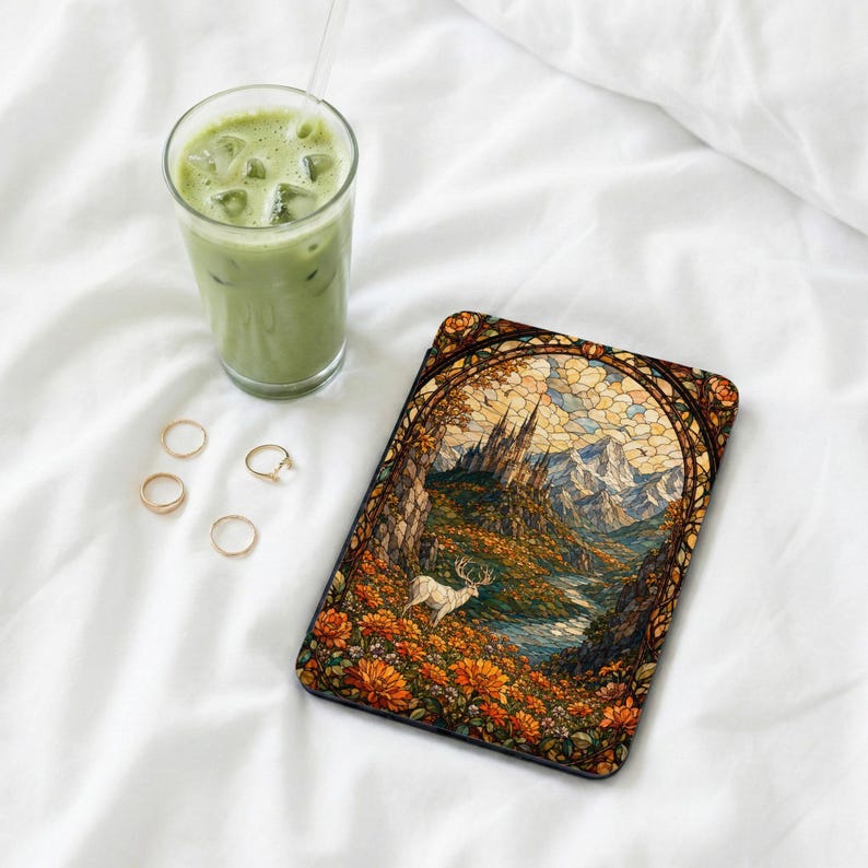 Case with stained glass art of castle, mountains, deer, and flowers next to iced matcha latte.