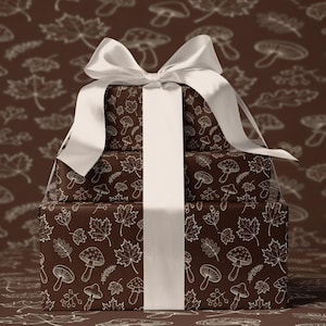 Puede incluir: Tres cajas de regalo apiladas envueltas en papel marrón con un patrón de setas y hojas blancas. Una cinta blanca ancha y un lazo aseguran los regalos. El fondo es marrón a juego con un patrón similar.