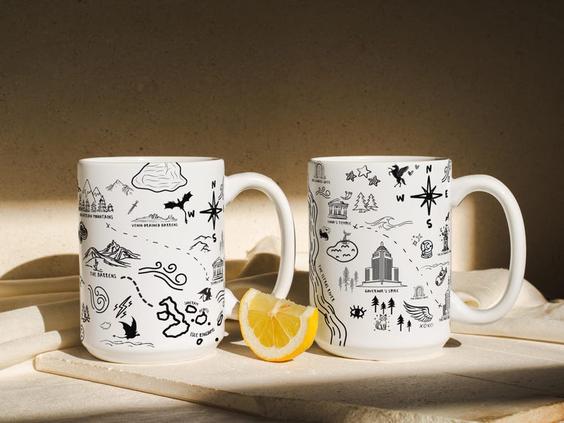 Two white mugs with black illustrations and text on them, placed on a white surface with a slice of lemon in front of them.
