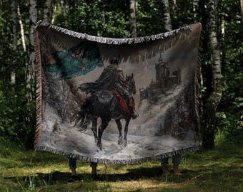 May include: A woven tapestry featuring a medieval knight on horseback, set against a snowy landscape with a castle in the background. The tapestry has a fringed edge and a color palette of black, gray, and teal.