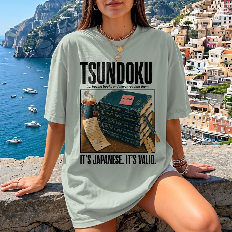 T-shirt with "Tsundoku" and a stack of unread books with receipts.