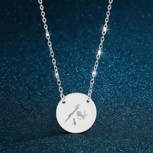 May include: A silver necklace with a circular pendant displaying etched designs. The pendant features a lightning bolt, a dragon, and two birds. The chain is delicate and sparkles against a dark blue backdrop.