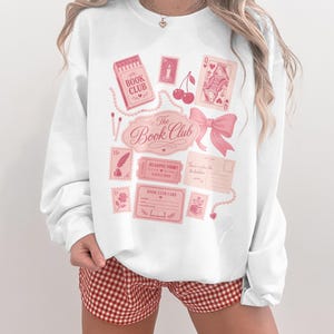 Pink sweatshirt with "The Book Club" graphics including cherries and playing cards.