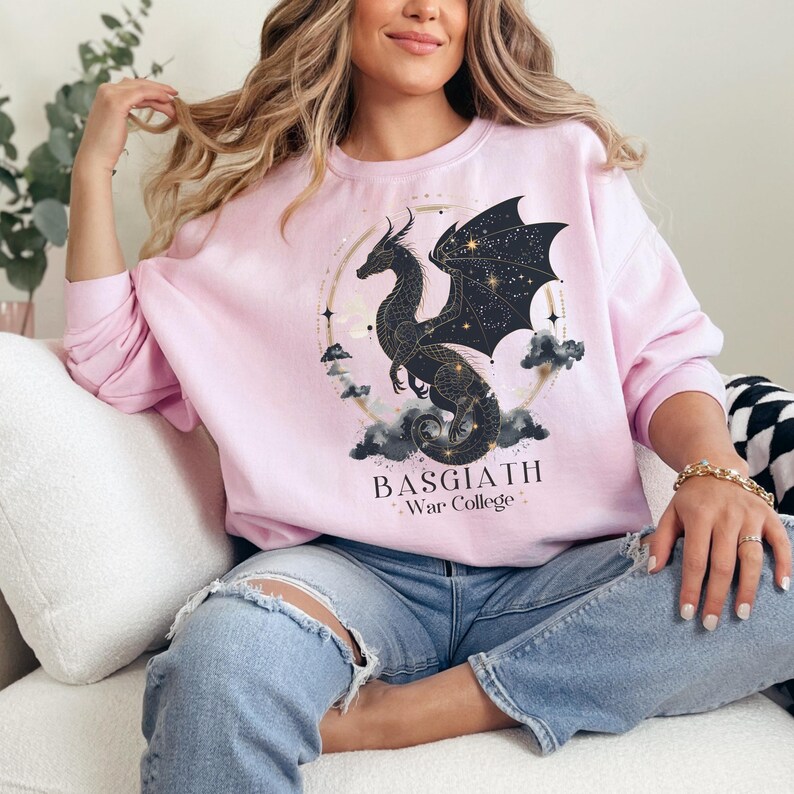 a woman sitting on a couch wearing a pink sweatshirt with a black dragon on it