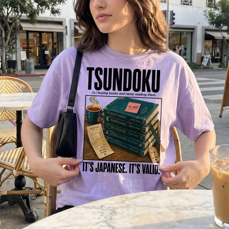 Purple t-shirt with "Tsundoku" text and stack of books graphic.
