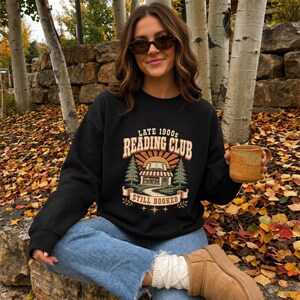 Black sweatshirt with "Late 1900s Reading Club Still Booked" graphic.