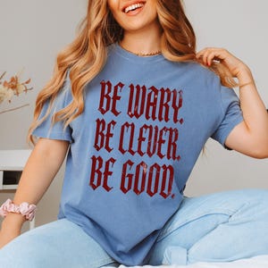 Blue t-shirt with red gothic text "Be wary. Be clever. Be good."