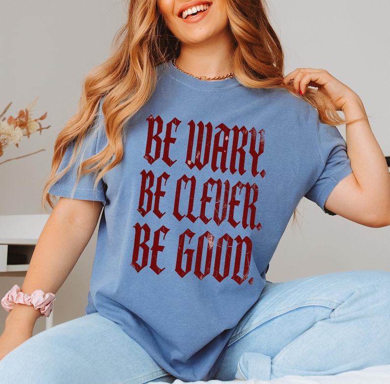 Blue t-shirt with red gothic text "Be wary. Be clever. Be good."