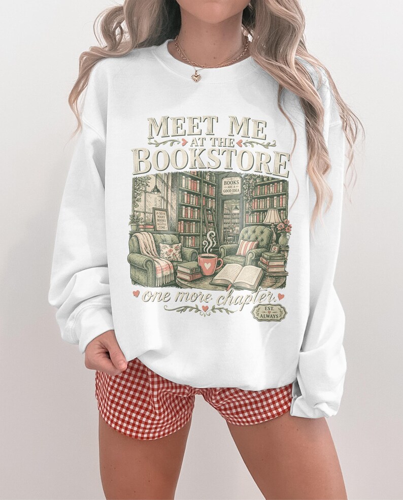 White sweatshirt with "Meet Me at the Bookstore" text and cozy library graphic.