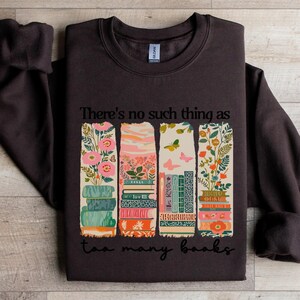 Dark brown sweatshirt with stacked books and floral design, reading "There's no such thing as too many books".