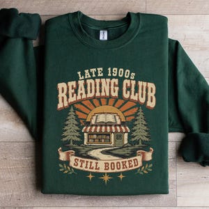 Green sweatshirt with "Late 1900s Reading Club Still Booked" graphic.