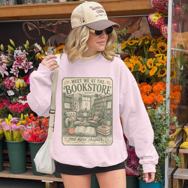 Pink graphic sweatshirt with "Meet Me at the Bookstore" text and library scene.