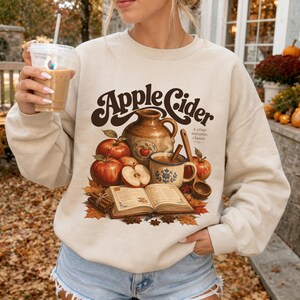 Crewneck sweatshirt with "Apple Cider" graphic, apples, pitcher, mug, and open book.