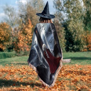 A person wearing a witch's hat and a cape with a dragon design is walking through a field of fallen leaves.