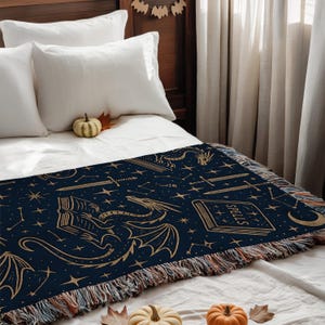 a bedroom with a bed covered in a blue and gold dragon-themed blanket. The bed is set against a wooden headboard, and there are white pillows on the bed. The room also has a window with white curtains, and there are some pumpkins and a book on the bed.
