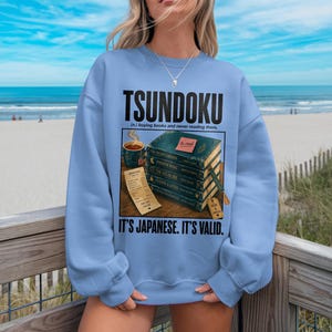 Light blue sweatshirt with "TSUNDOKU" and book stack graphic.