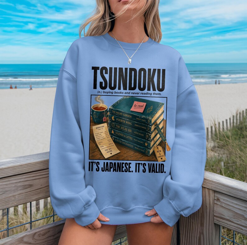 Light blue sweatshirt with "TSUNDOKU" and book stack graphic.
