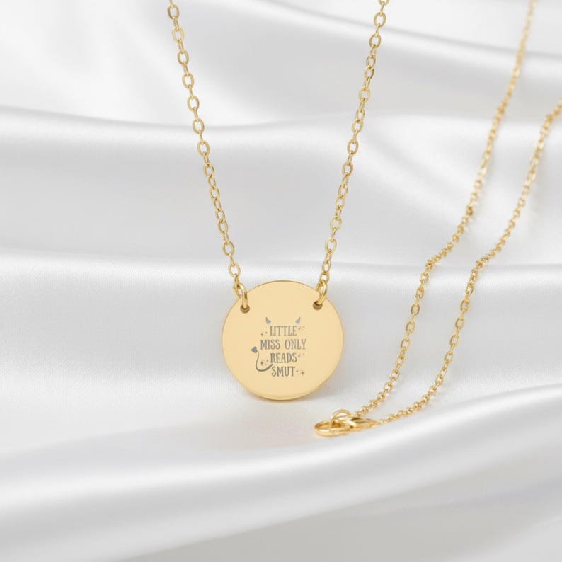 A gold-colored necklace with a round pendant featuring a message engraved on it.